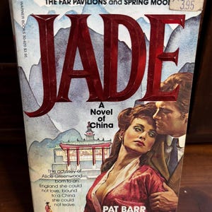 May include: A vintage paperback book titled "JADE" with a cover illustration of a woman and man embracing. The cover features the text "A Novel of China" and the author's name, Pat Barr. The book is a Warner Books edition.