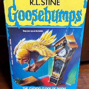 May include: A vintage paperback book titled "Goosebumps: The Cuckoo Clock of Doom" by R.L. Stine. The cover features a yellow and orange bird perched on a wooden beam, with a grandfather clock in the background. The book has a blue background.
