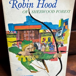 May include: Vintage book cover for "Robin Hood of Sherwood Forest" by Ann McGovern. The cover features an illustration of Robin Hood aiming an arrow, with a backdrop of a medieval town and the book's title in blue script.
