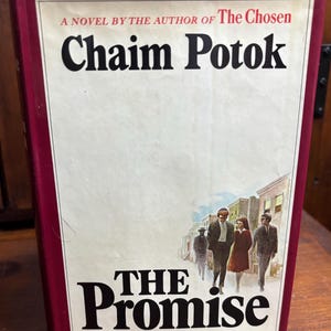 May include: A hardcover book titled "The Promise" by Chaim Potok. The cover features a drawing of four people walking on a street, with the title in large, bold letters. The book has a burgundy border.