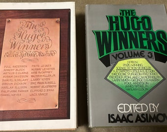 May include: Two book covers with the title "The Hugo Winners" in green and black lettering. The first book is volume 1 and features a copper plaque with the names of the Hugo Award winners. The second book is volume 3 and features a green and black design with the names of the Hugo Award winners.