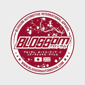 May include: A maroon circular sticker featuring white text and graphics. The text reads "BLOSSOM AUTOMOTIVE INTERNATIONAL APPAREL" around the edge, with "BLOSSOM" in a bold font in the centre. Japanese text and flags are also present.
