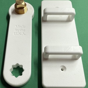 May include: Two white plastic tools. One has a brass fitting and the text "Made in the U.S.A." The other is a white rectangular piece with two handles. The tools are likely for a specific mechanical purpose.