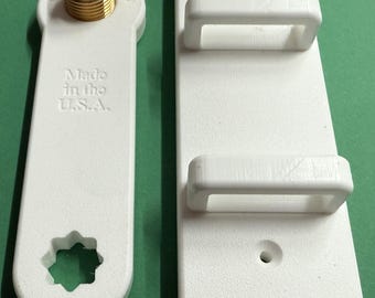 Könnte beinhalten: Zwei weiße Kunststoffwerkzeuge. Eines hat einen Messinganschluss und den Text "Made in the U.S.A.". Das andere ist ein weißes rechteckiges Teil mit zwei Griffen. Die Werkzeuge sind wahrscheinlich für einen bestimmten mechanischen Zweck bestimmt.
