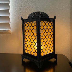 May include: A black metal table lamp with a geometric patterned shade. The lamp is lit and casting a warm glow.