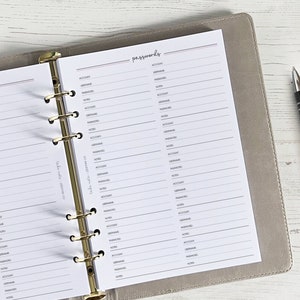 May include: A grey and white password log book with gold rings. The book has lines for writing down account names, usernames, passwords, and notes.