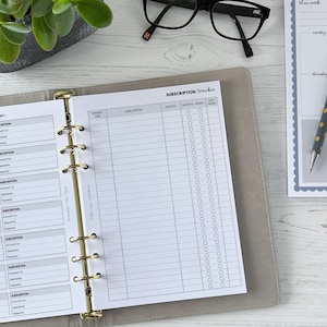 Op de afbeelding: Een grijze en witte abonnementstracker met een gouden binder. De tracker heeft secties voor accountinformatie, abonnementsdetails en een maandelijkse kalender met vinkjes.