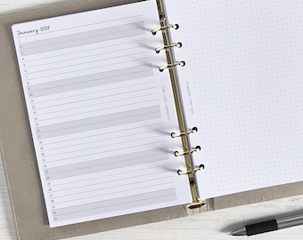May include: Open planner with a January 2027 calendar page and a dotted page. The calendar page has horizontal lines for each day of the month. The planner is open to reveal the pages and a pen is visible.