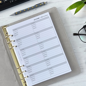 May include: A grey and white planner with gold rings. The planner has a page labelled "Account Information" with sections for company, account number, username, and password.