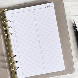 Puede incluir: Una página de lista de tareas blancas con un archivador dorado y un bolígrafo negro. La página tiene un encabezado que dice "to do list" y está dividida en dos columnas con casillas de verificación y líneas para escribir.