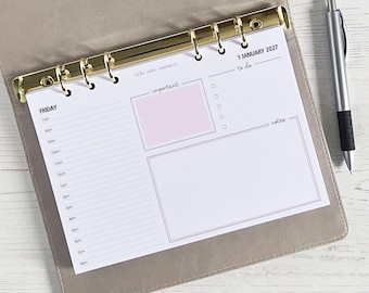 May include: A planner insert with a gold binder, featuring a daily schedule, to-do list, and notes section. The insert includes a pink box for important notes and the date "1 January 2027". A silver pen with a black grip rests beside the planner.