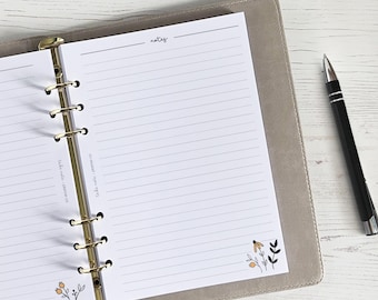 Pode incluir: Um planejador branco com um fichário dourado e páginas pautadas. O planejador tem uma seção rotulada como "notas" e um pequeno desenho floral no canto inferior direito.