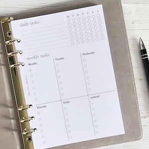 May include: A white planner page with a daily and weekly task list. The daily task list has a grid of 28 circles for ticking off tasks. The weekly task list has a grid of 12 squares for ticking off tasks. The days of the week are labelled at the top of the page.