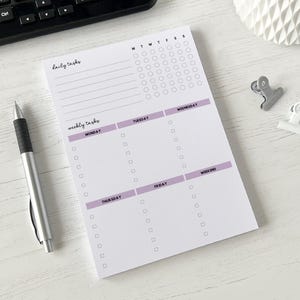 May include: A white notepad with a daily and weekly task list. The notepad has a purple header for each day of the week and a section for weekend tasks.