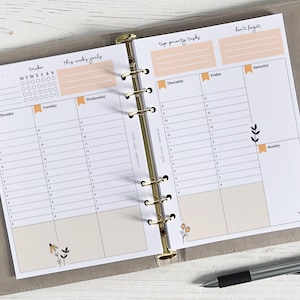 Può includere: Un planner settimanale con un calendario mensile, una sezione per gli obiettivi di questa settimana, le attività prioritarie e una sezione per non dimenticare. Il planner ha uno sfondo bianco con testo nero e linee. Il planner è aperto per mostrare i giorni della settimana, da lunedì a domenica.