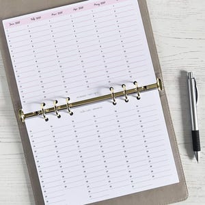 May include: A yearly planner open to a page showing January to May 2021. The planner is in a grey binder with gold rings. A silver pen with a black grip lies on the right. The calendar is in a ring binder.