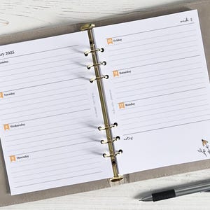 May include: A white planner with gold rings, open to January 2025. The left page shows the days of the week, Monday through Thursday, with space for writing. The right page shows Friday, Saturday, Sunday, and a notes section. The planner has a floral design in the bottom right corner.