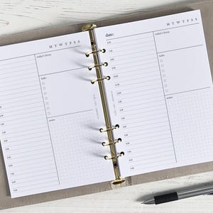 May include: A white daily planner with a gold binder. The planner has a daily schedule on the left side and a section for tasks and notes on the right side. The planner is open to a page with the date and the words "today's focus".