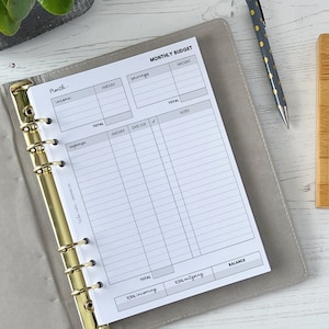 May include: A white monthly budget planner with sections for income, expenses, savings, and notes. The planner is open to a page with a grid for tracking expenses and income.