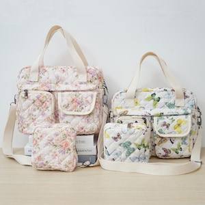May include: Two quilted tote bags with floral and butterfly patterns. Both bags have a zipper closure, multiple pockets, and a detachable shoulder strap. The floral bag is pink and white, while the butterfly bag is white with green and blue butterflies.