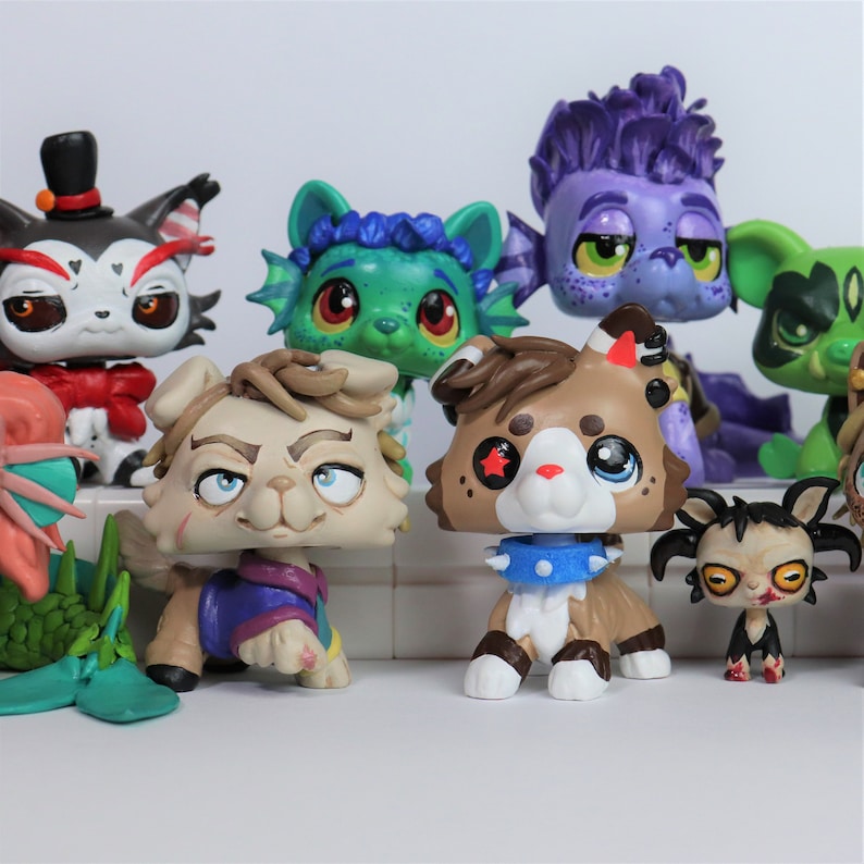 May include: A collection of stylized animal figurines featuring various characters with distinct painted details, including a black and white cat in a top hat, a green aquatic creature, a purple monster, and several brown and tan canine figures.