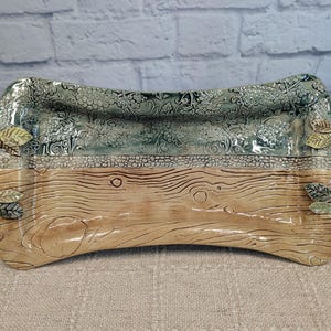 May include: A rectangular ceramic serving tray with two curved handles. The top half features a textured green grape vine pattern, while the bottom half displays a tan wood grain design. Small sculpted leaves accent the base of each handle.