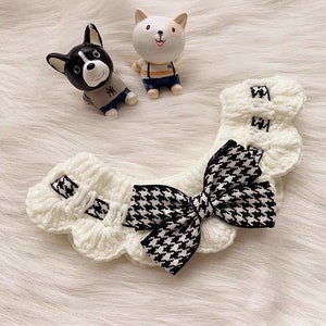 May include: White crocheted pet collar with a black and white houndstooth bow. The collar has a scalloped edge and is decorated with a small black and white ribbon.