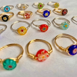 Peut inclure: Une collection de 16 bagues en fil de fer avec des perles de verre florales. Les bagues sont faites de fil d'argent et d'or et présentent une variété de couleurs, notamment le bleu, le rouge, le vert, le jaune et le noir.
