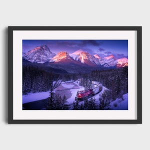May include: A framed landscape photograph of a train winding through a snowy mountain valley. The train is red and white, and the mountains are lit by the setting sun. The sky is a mix of purple and blue.