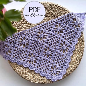 May include: A crocheted lavender-colored scarf with a scalloped edge, displayed on a woven straw mat. The text "PDF pattern" is visible on a white circle.