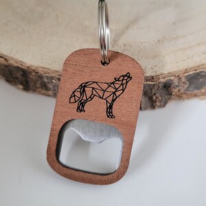 Op de afbeelding: Houten flessenopener sleutelhanger met een geometrisch wolf ontwerp. De opener is bruin en heeft een zilveren metalen flessenopener.