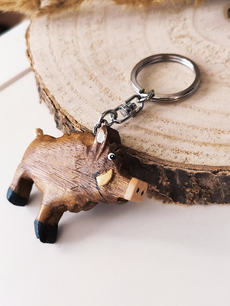 May include: A wooden boar keychain with a brown and black painted design. The keychain has a silver metal ring and chain.