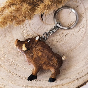 May include: Wooden boar keychain with a brown and black painted finish. The keychain has a silver metal ring and chain.