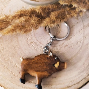 May include: A wooden boar keychain with a brown body, black hooves, and a white tusk. The keychain is attached to a silver key ring.