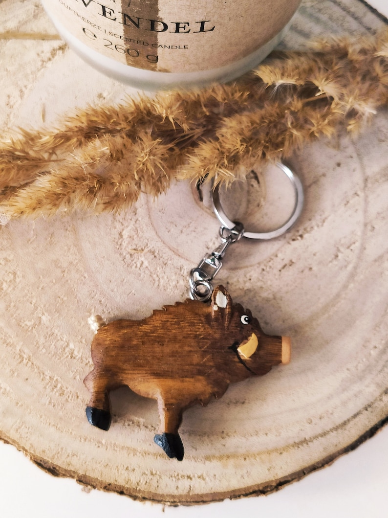 May include: A wooden boar keychain with a brown body, black hooves, and a white tusk. The keychain is attached to a silver key ring.
