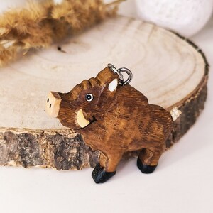 May include: A wooden wild boar keychain with a brown body, black hooves, and a white tusk. The keychain has a silver loop for attaching to a bag or keys.