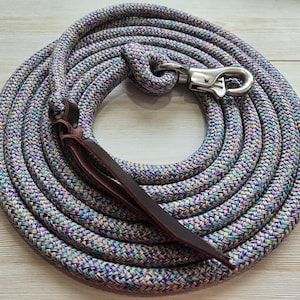 May include: Coiled multi-colored rope with a silver-colored clasp and a brown leather strap. The rope is a mix of purple, blue, and green hues. The leather strap is attached to the rope, and the clasp is at the end.
