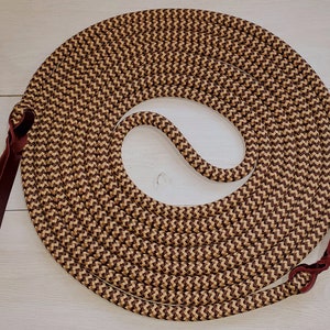 May include: A brown and tan braided rope with burgundy leather ends. The rope is coiled in a circle and the ends are tied together.