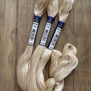 Peut inclure: Trois bobines de fil à broder DMC de couleur écru. Les bobines sont étiquetées avec les numéros 20, 25 et 30, et chaque bobine contient 10 grammes de fil.
