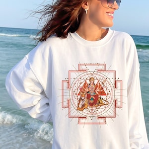 May include: White sweatshirt with a red and gold graphic of a Hindu goddess with a tiger on each side. The graphic is surrounded by a geometric design.