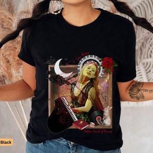 May include: Black t-shirt with a graphic print of a woman playing a piano with a crescent moon, clouds, a cross, a red rose, and a rabbit. The text "The Return Sound of Silence" is printed below the graphic.