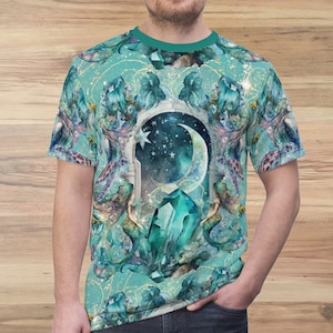 May include: A teal blue t-shirt with a graphic print of a crescent moon, stars, and a large crystal in a turquoise and green color scheme. The background is a light teal blue with gold glitter.