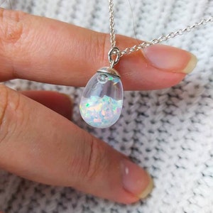 May include: A silver chain necklace with a teardrop-shaped pendant filled with iridescent opal flakes.