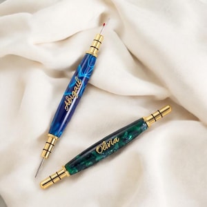 May include: Two personalized threaders with gold accents. One is blue with the name Abigail and the other is green with the name Olivia.