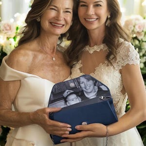 May include: A navy blue clutch with a silver chain strap. The clutch is open, revealing a black and white photograph. Two women are smiling, one in an off-the-shoulder white dress and the other in a white dress with lace detailing.