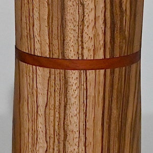 May include: A wooden cylinder with a brown and tan striped pattern. The cylinder has a thin red band around the middle.