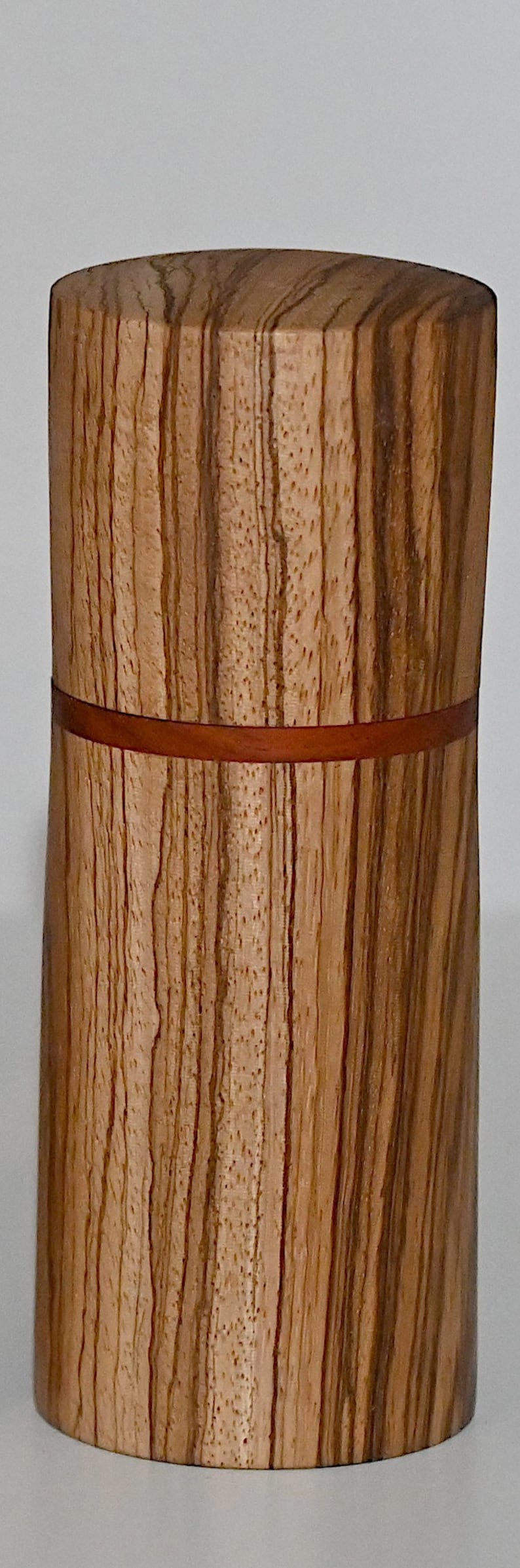May include: A wooden cylinder with a brown and tan striped pattern. The cylinder has a thin red band around the middle.