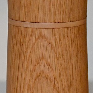 May include: A wooden container with a natural wood finish. The container has a smooth, rounded top and a slightly flared bottom. The wood grain is visible and adds a rustic touch.