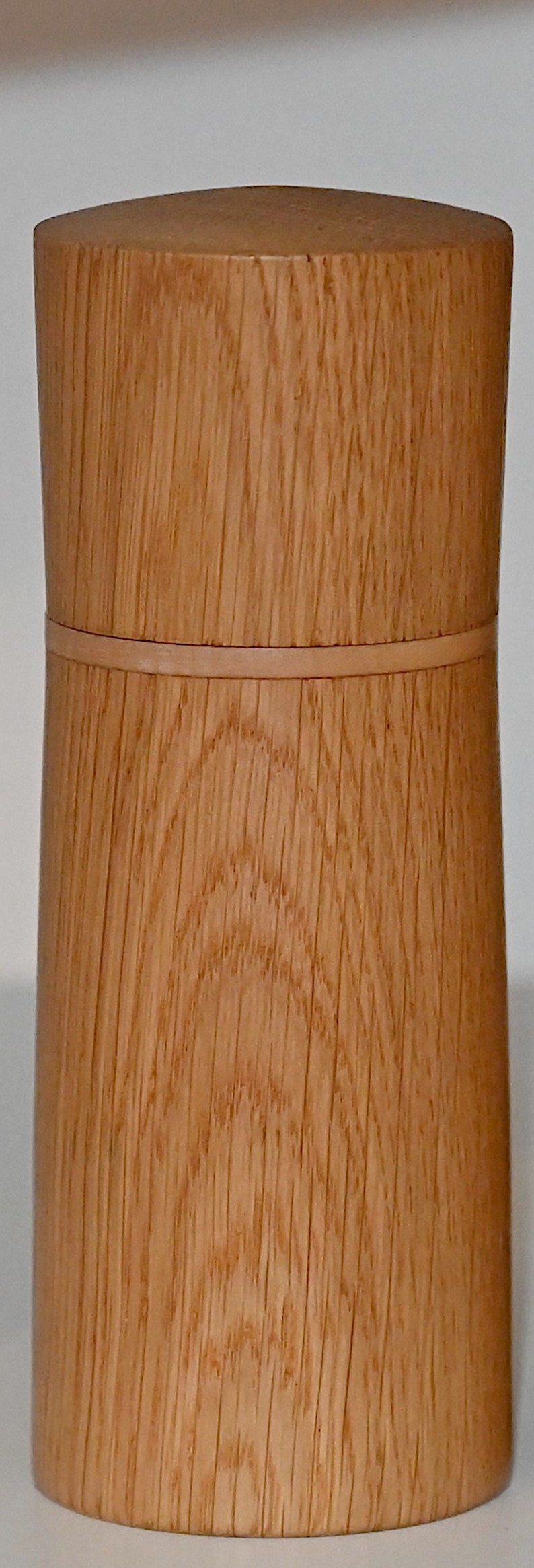 May include: A wooden container with a natural wood finish. The container has a smooth, rounded top and a slightly flared bottom. The wood grain is visible and adds a rustic touch.