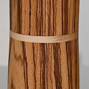 May include: A cylindrical wooden box with a natural wood grain pattern and a light brown band around the middle.